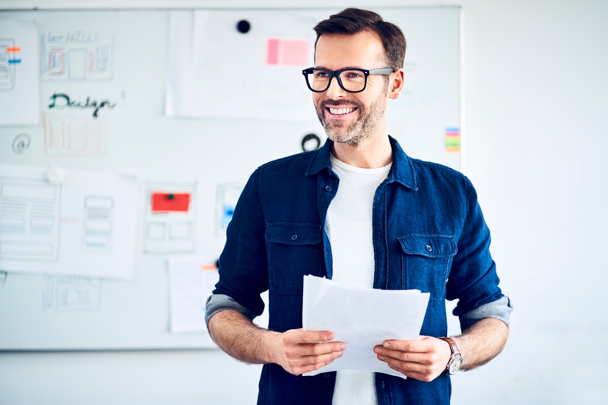 Smiling businessman with papers standing at whiteboard leading a presentation