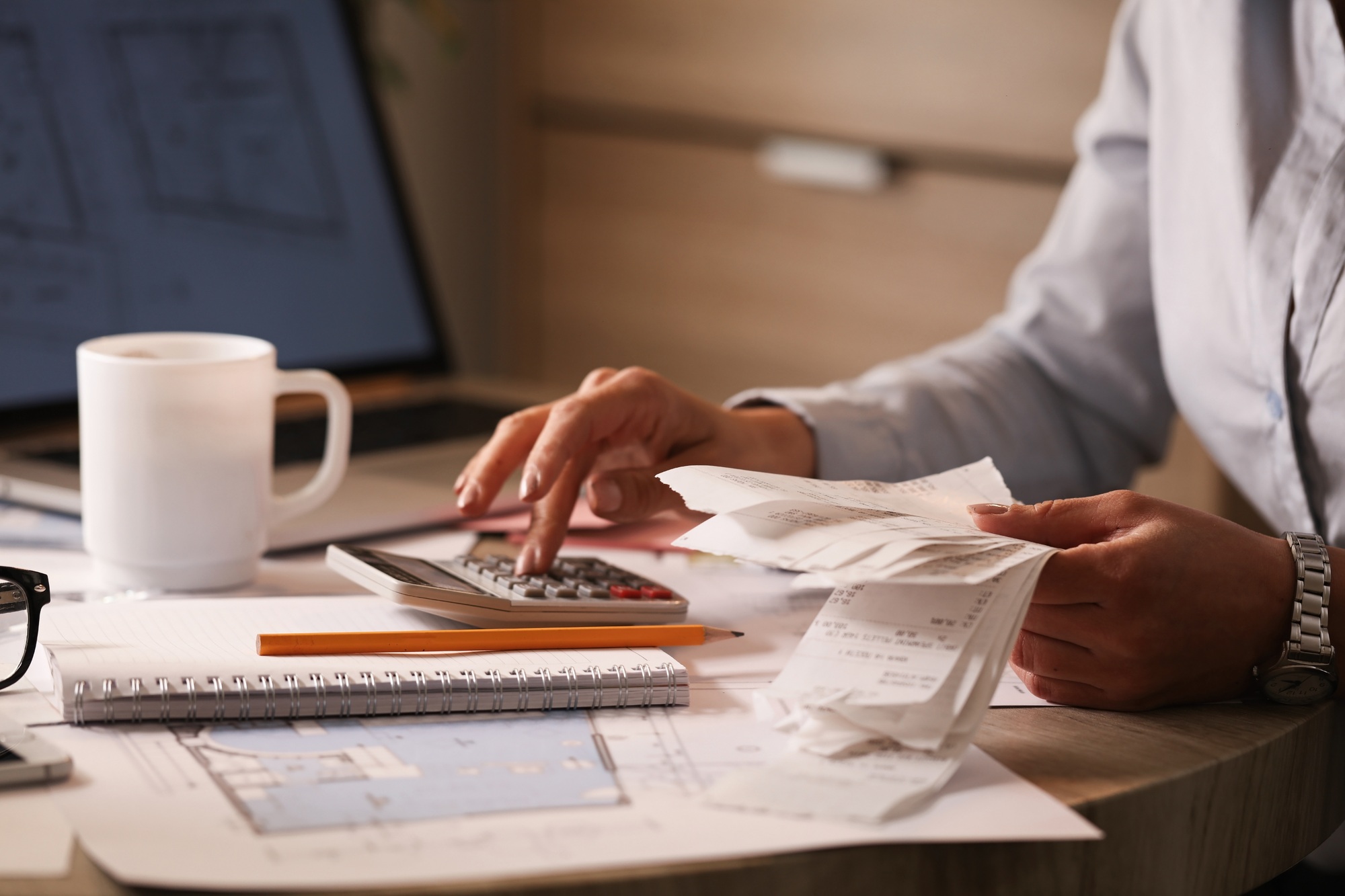 Unrecognizable entrepreneur planning her business budget and using calculator in the office.