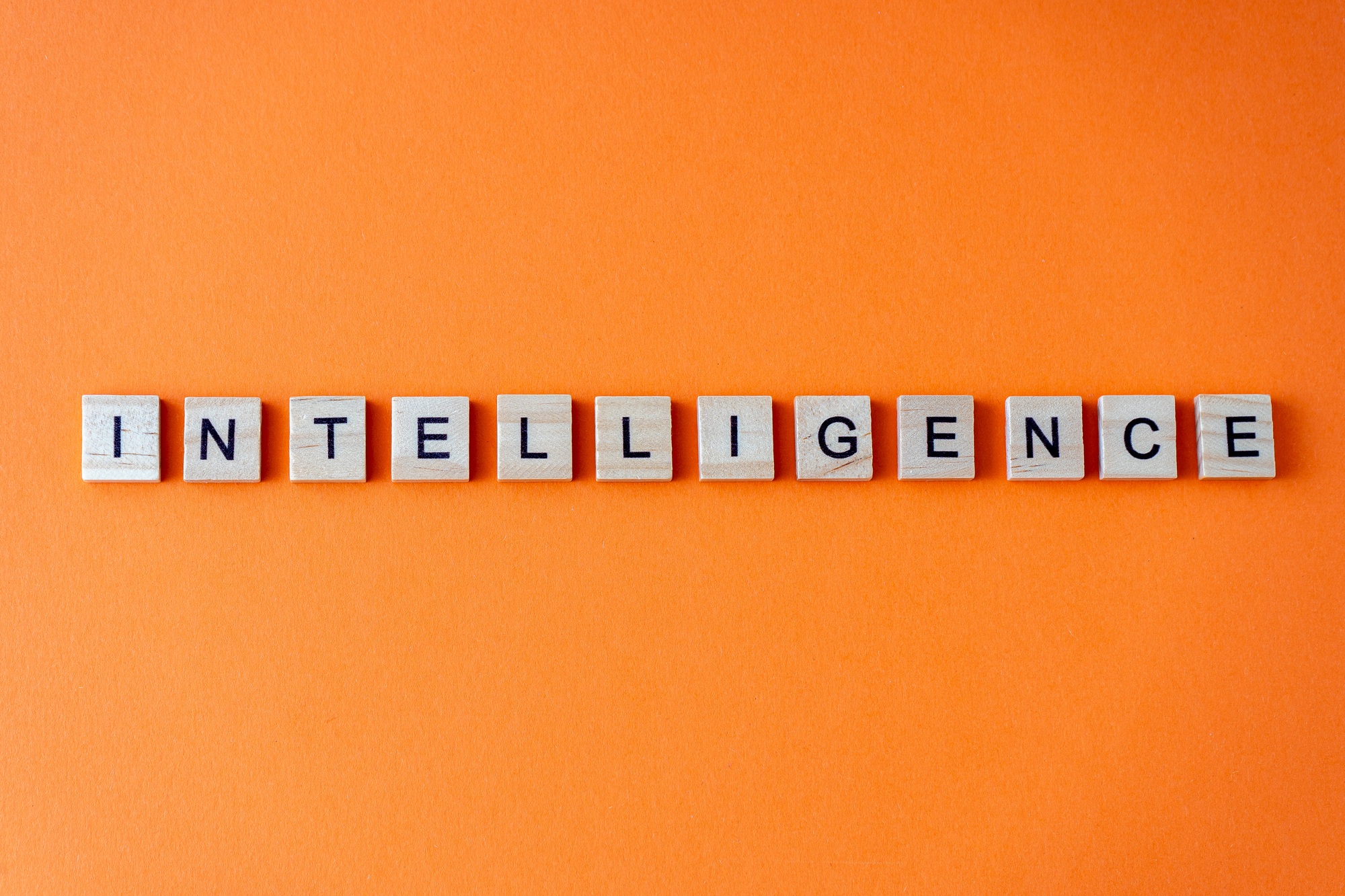 Word intelligence. The phrase AI is laid out in wooden letters top view. Orange flat lay background.