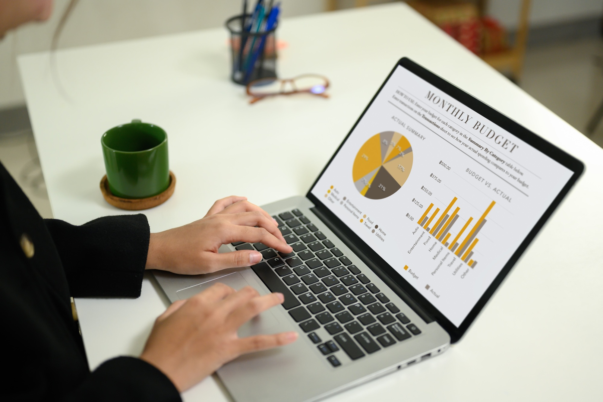 Hand using laptop displaying a comprehensive monthly budget report with graphs and analytics