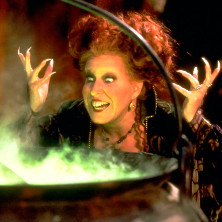 Person in spooky, theatrical costume and makeup, standing over a bubbling cauldron, gesturing dramatically with raised hands
