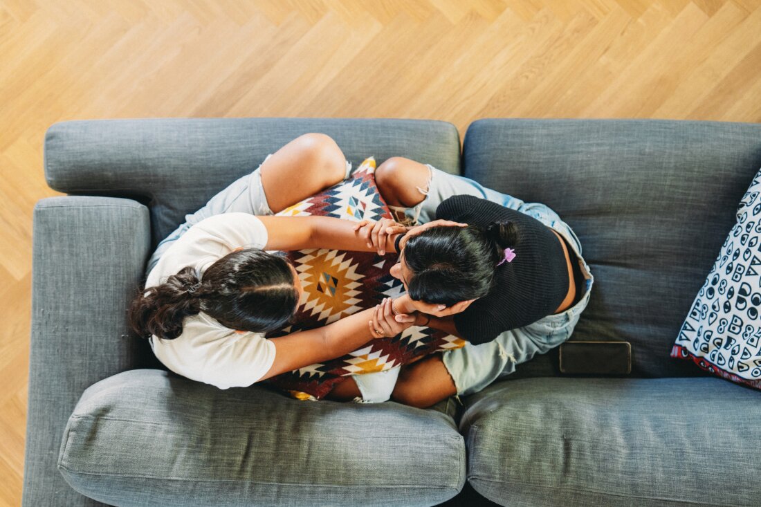 Teenage girl comforting sad friend on couch at home, showing empathy and compassion. Image captures genuine care and understanding between young women