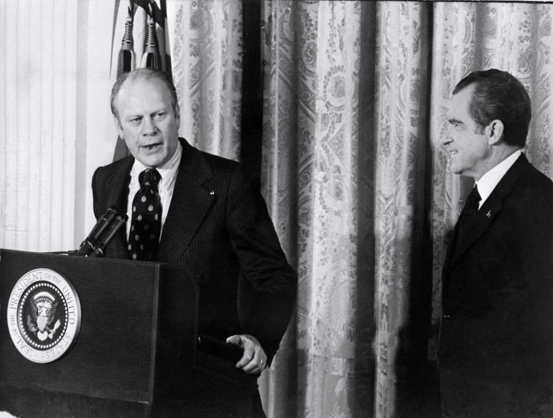 President Gerald Ford (L) talks at a podium as President Richard Nixon (R) stands nearby.