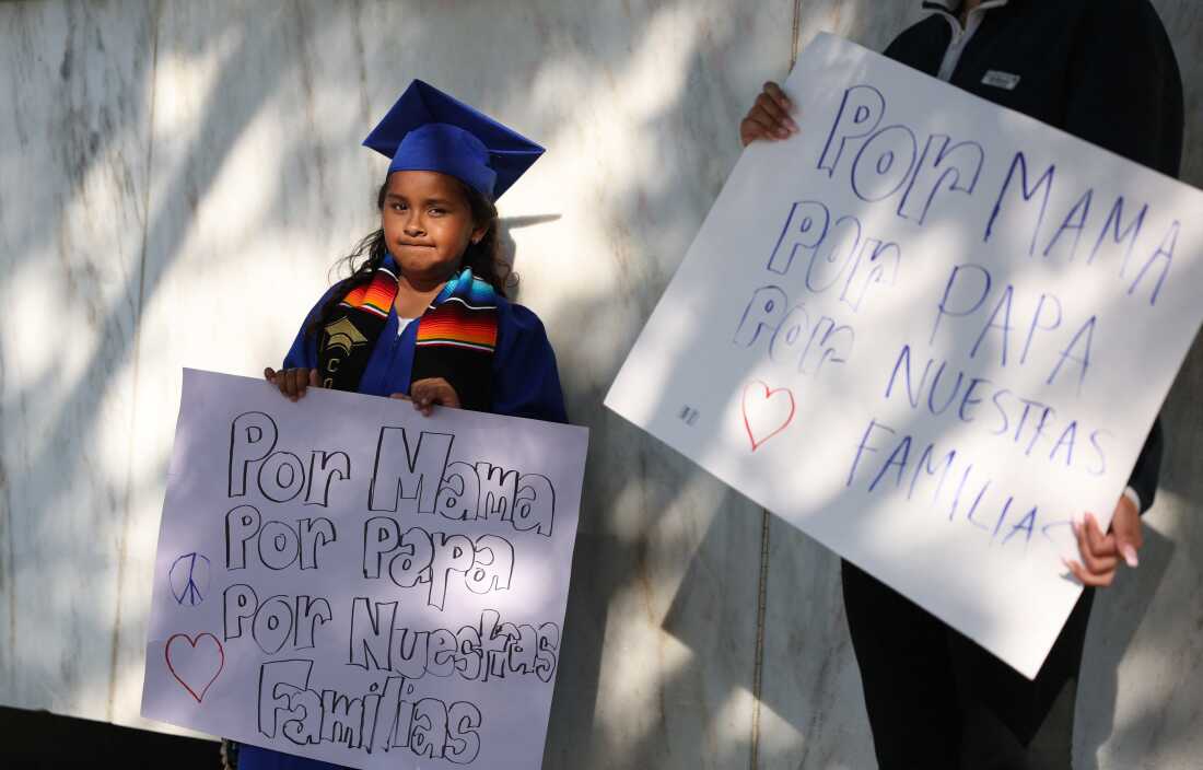 An 8-year-old second grade student, born in the US to an undocumented family, stands holding a sign in her graduation cap and gown after her school ceremony, outside the Federal Building as protests continue in response to federal immigration operations in Los Angeles on June 10, 2025.