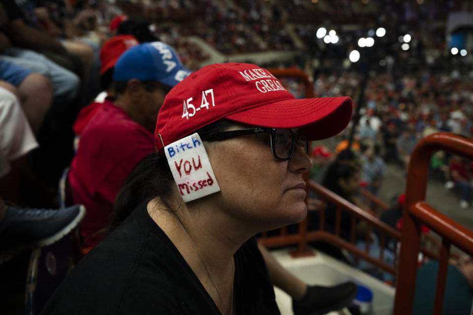 Person in a "Make America Great Again" cap with a sign attached that reads "Bitch you missed" at a crowded event