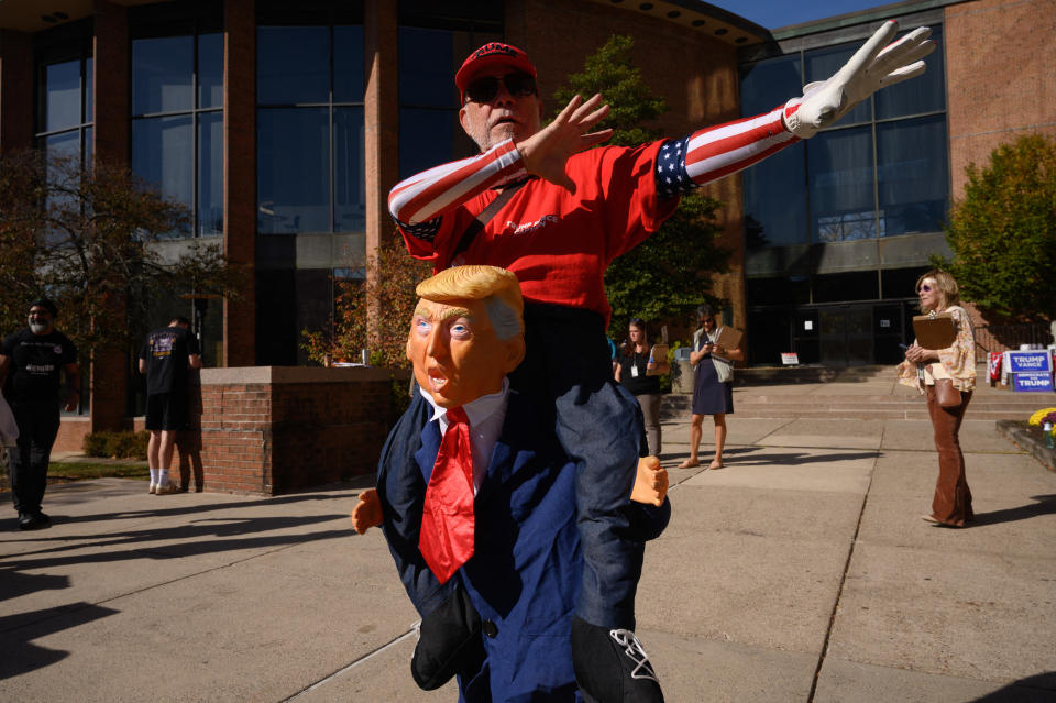 Person in a costume appearing to ride a figure resembling Trump, with a patriotic sleeve and matching hat, posing outdoors