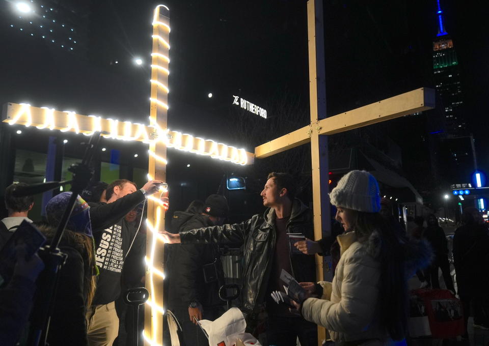 People gather at night, holding and standing near large illuminated crosses, engaged in conversation or distributing pamphlets