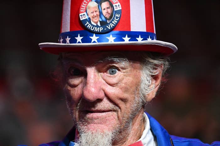 Man wearing a star-spangled top hat with political campaign button featuring faces of two men. He has an expressive, engaged look
