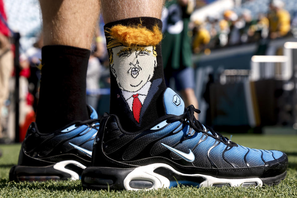 Person wearing sneakers with socks depicting a cartoonish face with distinctive hair on a sports field