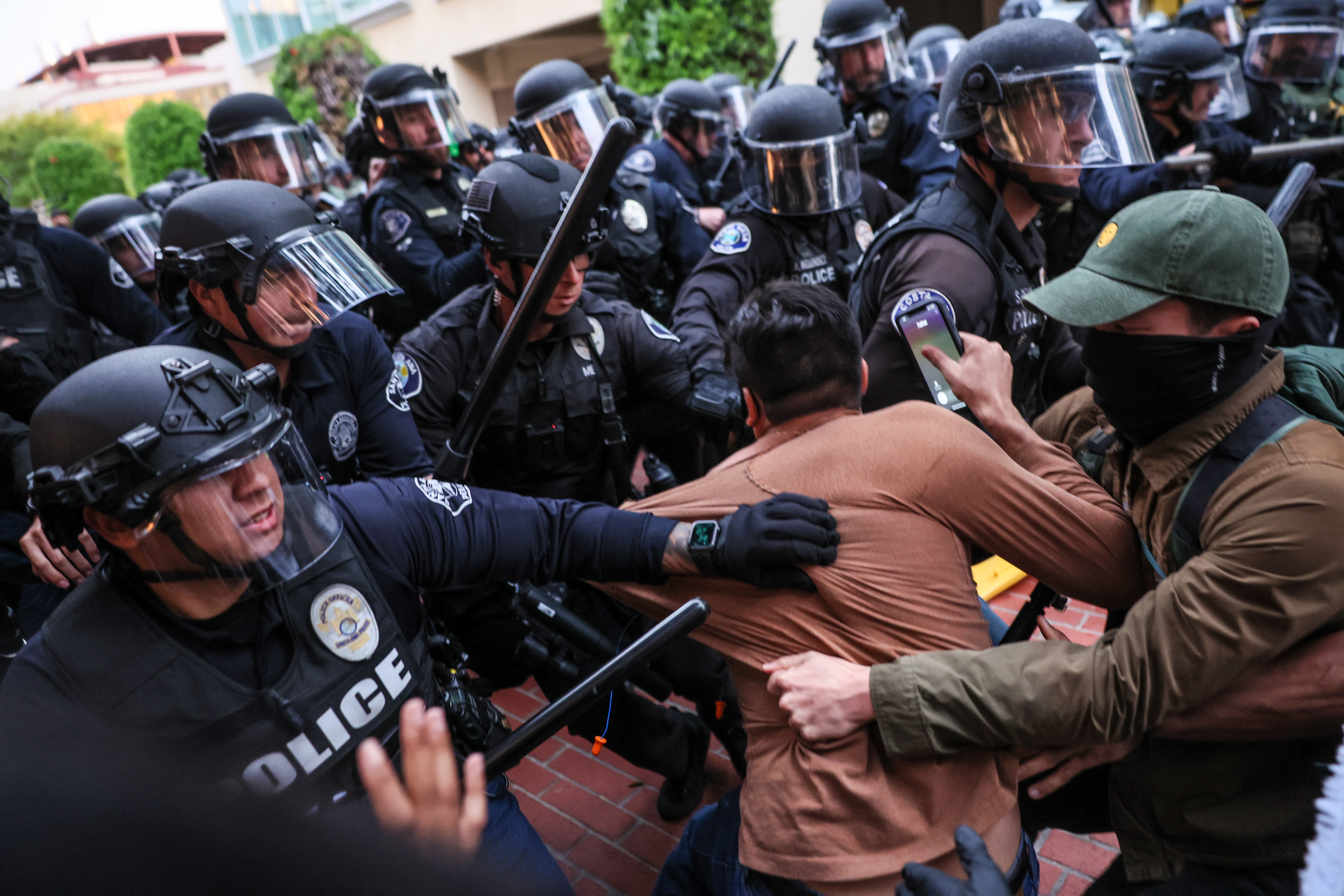 Irvine, CA, Wednesday, May 15, 2024 - Police grab a protester as they move forward to break up a demonstration at UC Irvine. Scores of law enforcement personnel from various agencies move hundreds of demonstrating students, faculty and supporters protesting the treatment of Palestinians and the UC system's investments in Isreali interests. (Robert Gauthier/Los Angeles Times via Getty Images)