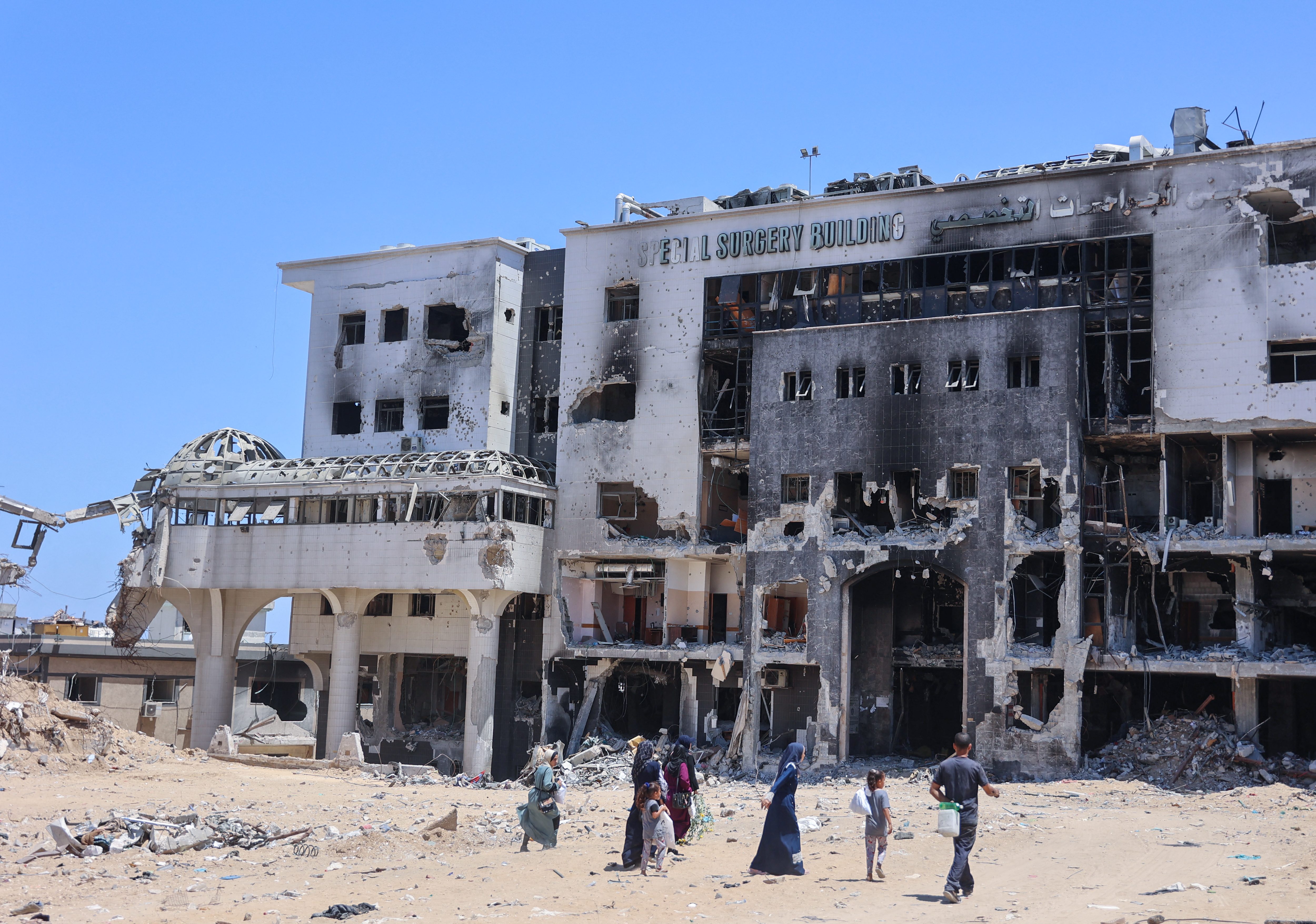 People walk towards a devastated building at Al-Shifa hospital in Gaza City on June 11, 2024. Israeli troops conducted raids in November and March on Al-Shifa hospital, amid the ongoing conflict between Israel and the Palestinian Hamas militant group. The medical facility, the largest in the Gaza Strip, was reduced to rubble after an Israeli operation in March, the WHO said. (Photo by Omar AL-QATTAA / AFP) (Photo by OMAR AL-QATTAA/AFP via Getty Images)