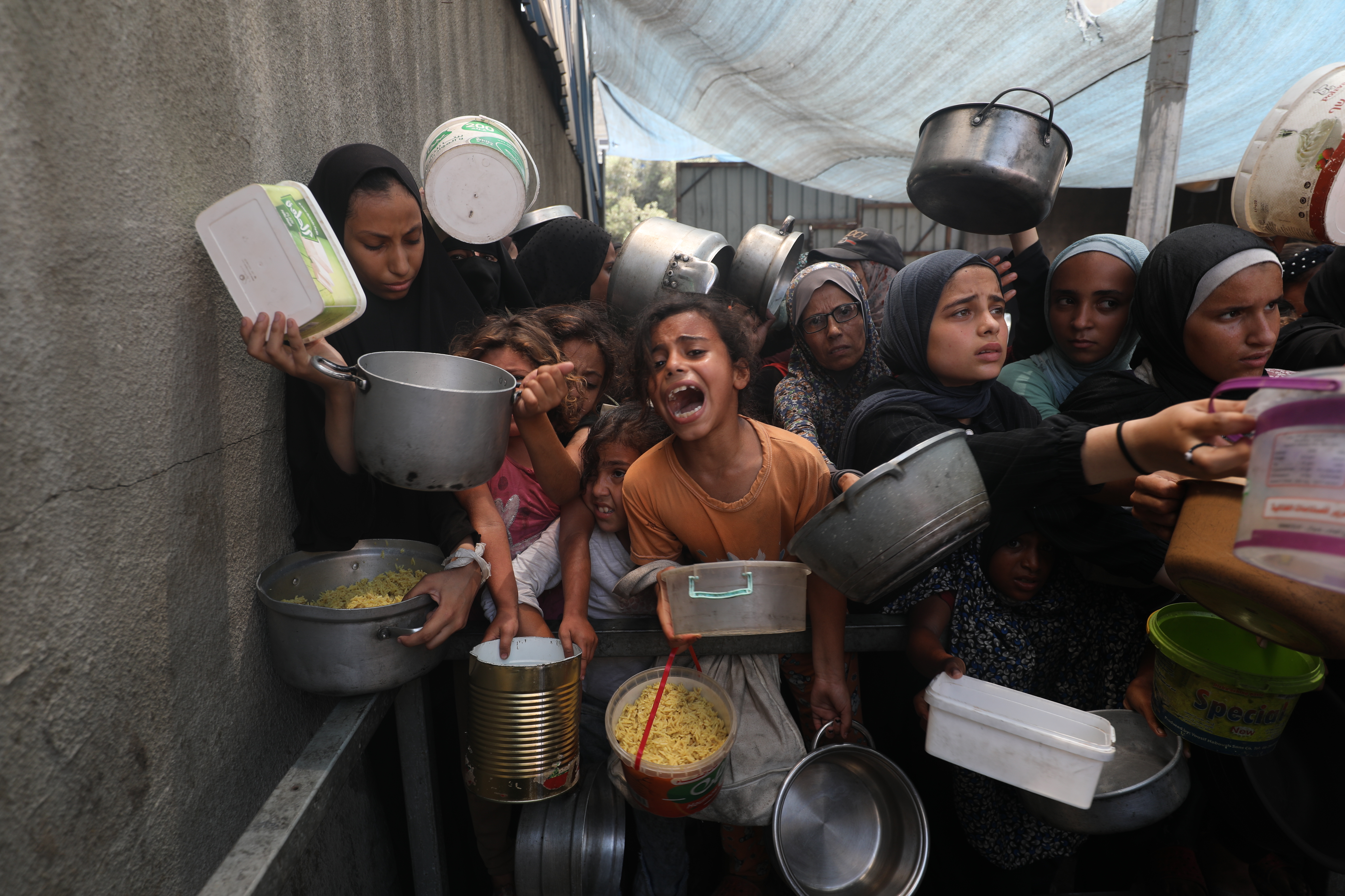 DEIR AL-BALAH, GAZA - AUGUST 18: Palestinians, including children, who are struggling to access food due to Israel's blockade and ongoing attacks on the Gaza Strip, wait in line to receive hot meals distributed by the charity organization at the Nuseirat refugee camp in Deir al-Balah, Gaza on August 18, 2025. There was a concentration in the area during the hot meal distribution. (Photo by Moiz Salhi/Anadolu via Getty Images)